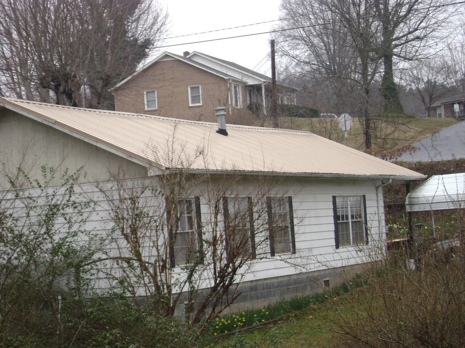 Tan metal roof on a white sided house set into a hillside — Commercial Roofing by Roofing Brothers in Adams