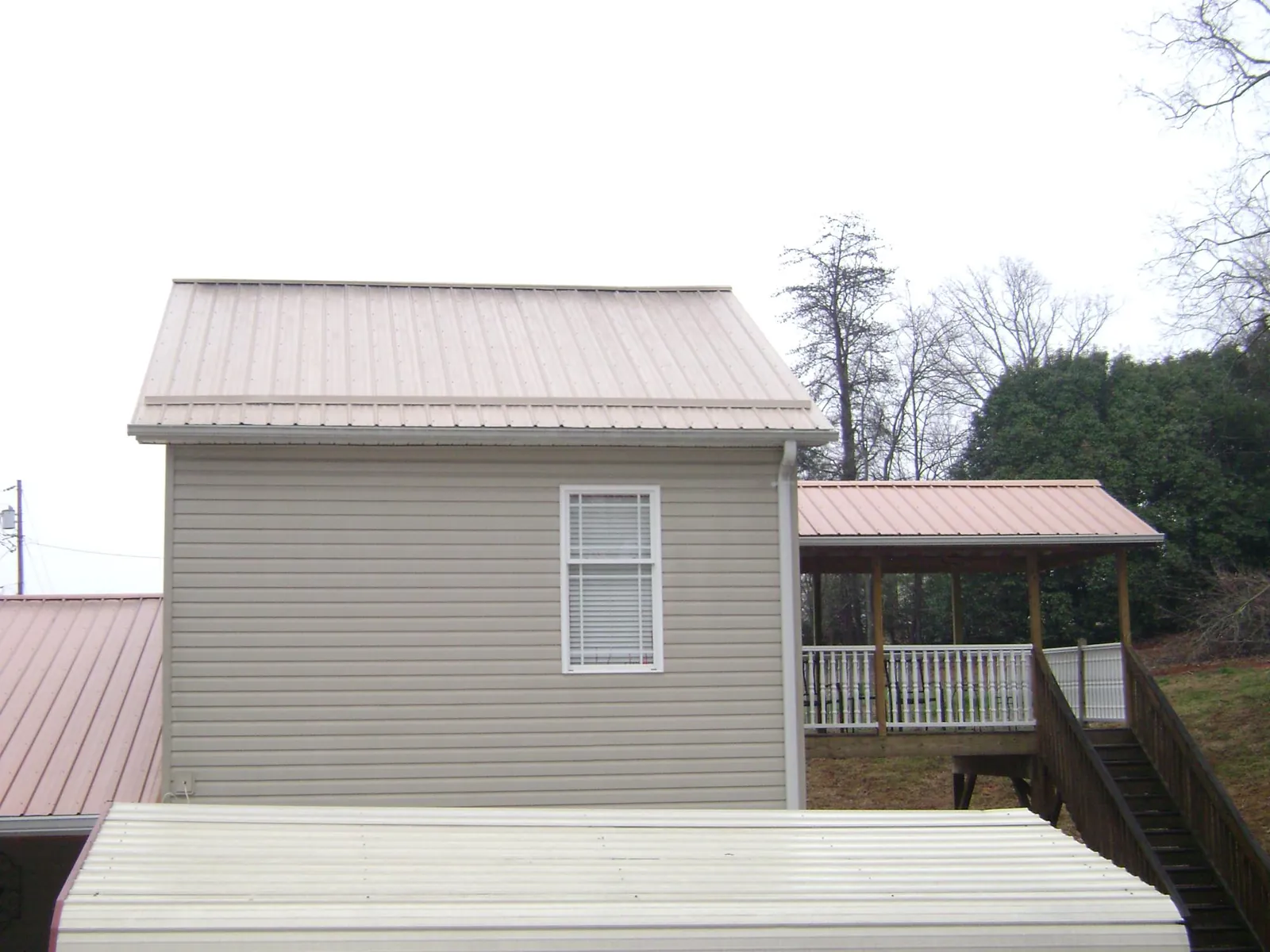 Tan metal roofs on a two story addition and attached porch, from a Roof Replacement job in Adams